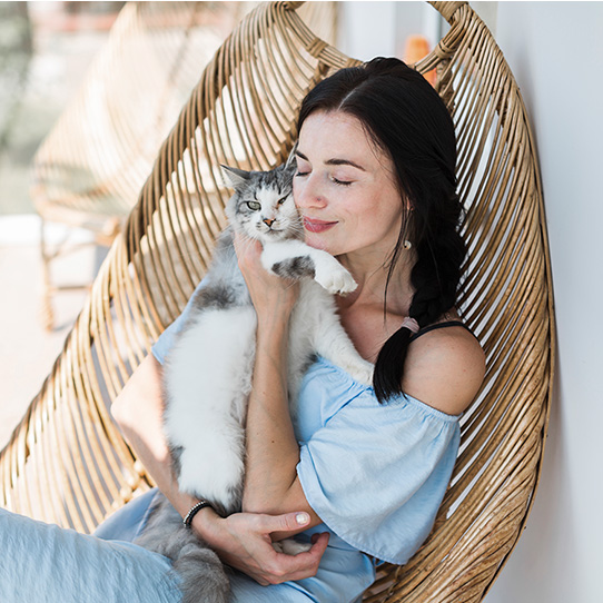 a woman sits outside on a patio and hugs her cat